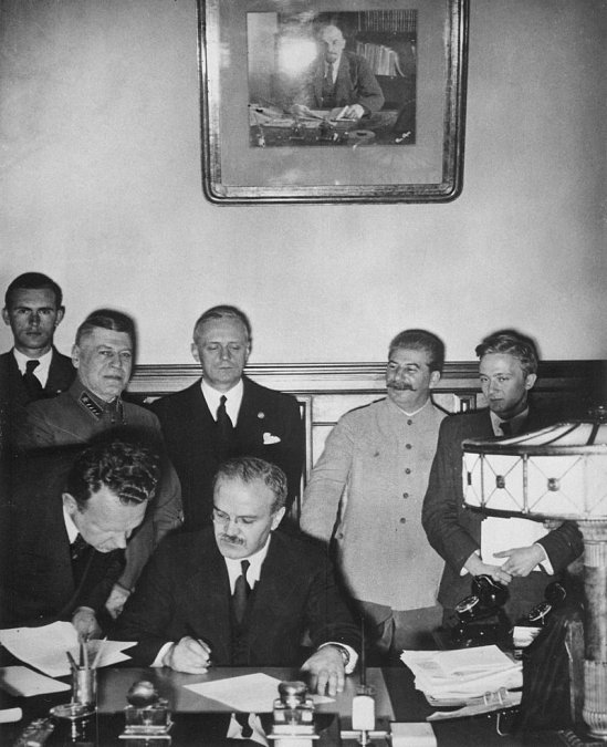 Firma del pacto. Mólotov está a punto de firmar. Tras él se encuentran Ribbentrop (con los ojos entrecerrados) y Stalin a su izquierda.