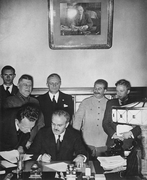Firma del pacto. Mólotov está a punto de firmar. Tras él se encuentran Ribbentrop (con los ojos entrecerrados) y Stalin a su izquierda.
