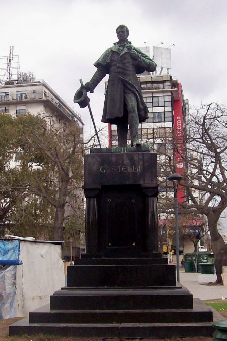 Juan José Castelli (1764 -1812) abogado, jurisconsulto, funcionario y político. Adhirió desde su época de estudiante a las ideas revolucionarias: integró el partido carlotista; luego fue decisiva su participación durante la semana de Mayo de 1810, cimentada en su condición de excelso orador. Fue vocal de la Primera Junta de gobierno y posteriormente nombrado como representante de la Junta en el Ejercito del Norte. Encabezó la primera expedición al Alto Perú y tras una serie de victorias preliminares fue derrotado en Huaqui en el año 1811, motivo por el cual fue enjuiciado. Sin embargo muere antes de ser sentenciado. Ironías del destino, el Orador de Mayo fallecería de cáncer de lengua. El Doctor Castelli, al cumplirse el primer centenario de la Revolución de Mayo, recibió su merecido homenaje en el bronce. Costeada por la Municipalidad de Buenos Aires, la escultura fue encomendada al artista Gustav Eberlein e inaugurada en un acto multitudinario celebrado el 20 de Mayo de 1910. El monumento se encuentra constituido por un basamento revestido en granito negro, el cual cuenta en sus laterales con dos relieves que describen escenas de la vida del orador de Mayo: a la izquierda se ubica la Intimación al Virrey Cisneros de presentar la renuncia, y a la derecha el momento de su discurso en el Cabildo Abierto del 22 de Mayo de 1810. Sobre el frente se halla grabado el nombre del homenajeado. Corona el pedestal la figura en bronce de Castelli vestido con levita y sosteniendo galera y bastón con su mano derecha. Su severo rostro evidencia la determinación e intrepidez que lo caracterizara como hombre de acción.